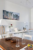 Blick von Holztisch auf weiße Küchenzeile und grossformatiges Foto