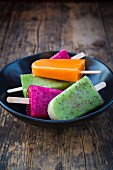 Various fruit ice lollies in a bowl on a wooden surface