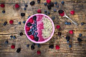A smoothie bowl with berries and hemp seeds on a wooden surface (seen from above)