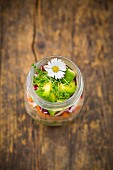 A layered salad in a jar with rice, vegetables and daisies (seen from above)