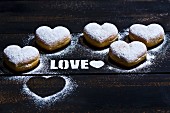 Heart-shaped doughnuts and the word Love in icing sugar on a wooden surface