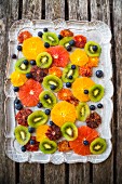 Sliced citrus fruits, kiwi slices and blueberries on a tray (seen from above)
