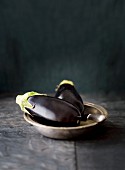 Two aubergines in a metal bowl with a knife