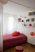 Ethnic bedspread in shades of red, white wall-mounted shelves and floating cabinet