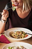 Frau isst Gemüsegericht und Salat an Tisch in Restaurant