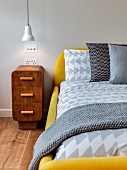 Antique bedside cabinet next to modern bed with yellow upholstered frame