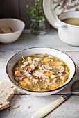 A bowl of lentil soup with ham and vegetables with bread