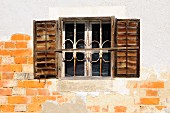 Old window with bars and shutters in façade wit crumbling plaster