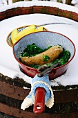 Kale with sausage in a saucepan outside on a snow covered wooden barrel