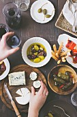 A mini buffet with the cheese platter, red wine, olives, vine leaves stuffed with rice, capers, peppers filled with feta cheese, and dried tomatoes