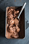 Partially melted chocolate ice cream with an ice cream scoop in a container