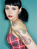 A black-haired woman with tattoos wearing a checked Rockabilly-style retro dress