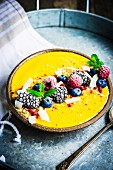 Smoothie bowl with mango, frozen berries, grated coconut and mint