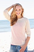 Dunkelblonde junge Frau in hellem Strickpulli und Jeans am Strand