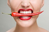 A woman biting on a chili pod