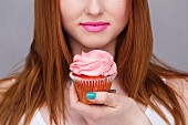 A young woman with long red hair holding a pink cupcake