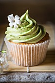 A cupcake with matcha frosting and a jasmine flower