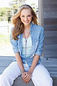 A young blonde woman wearing a light top, trousers and a denim blouse