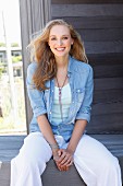 A young blonde woman wearing a light top, trousers and a denim blouse