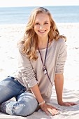 A young blonde woman on a beach wearing a long-sleeved beige shirt and jeans