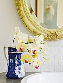 Yellow orchids in blue and white jug on washstand below mirror with carved frame