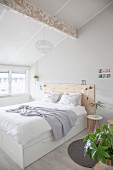 Double bed with wooden headboard in bright attic bedroom