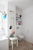 Pebble floor, toilet, wooden stool and mirror on wall in white bathroom