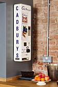 Old chocolate bar dispenser in kitchen in front of brick wall
