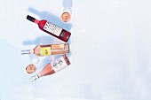 Three bottles of summery fruity rose wine on a white surface (seen from above)