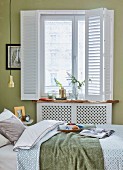 Frühstückstablett auf Bett und vor Fenster mti weißem Scheibenvorhang im Schlafzimmer mit grüngetönter Wand