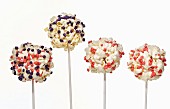 Four popcorn balls on sticks decorated with colourful sugar sprinkles
