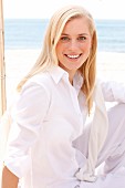 A young blonde woman on a beach wearing a white blouse and trousers