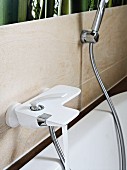 A white bath tap and a shower hose on a tiled wall