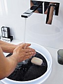 Washing over a white plastic bowl with a black base in a slate design and a wall-mounted designer tap