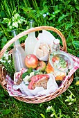 A picnic basket with salami sandwiches, salad, lemonade, apples and biscuits