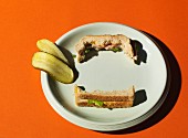 A half-eaten New York Deli sandwich and sliced gherkin on a white plate