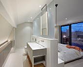 Moderner Schlafraum mit abgetrenntem Badbereich; Waschtisch an freistehender Brüstungswand mit Glasscheibe vor Doppelbett