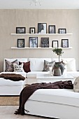 White sofa, accessories in earthy tones and pictures on narrow shelves on beige wall