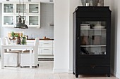 Black display cabinet in front of open-plan kitchen with dining area