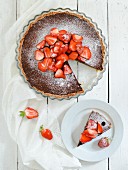 A chcolate tart topped with strawberries and icing sugar