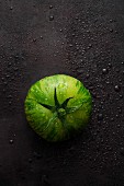 A green striped tomato on a black surface