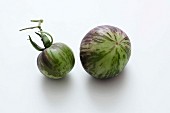 Two green striped tomatoes on a white surface