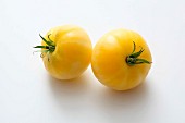 Two yellow tomatoes on a white surface