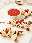 Pastry wrapped sausages with ketchup as Halloween mummies