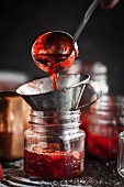 Strawberry jam being filled into a jar with a funnel