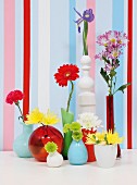 Collection of colourful vases holding various flowers in front of walls painted with vertical stripes