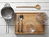 Assorted kitchen utensils: a sieve, a saucepan, cutlery, a small glass bowl and a measuring cup