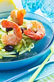 King prawns on a lemon and fennel salad with black olives on a glass turquoise plate