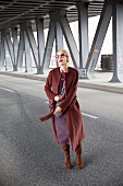 A blonde woman wearing a woollen coat, a leather dress, sunglasses and boots