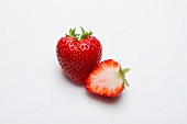A whole strawberry and half a strawberry on a white surface
